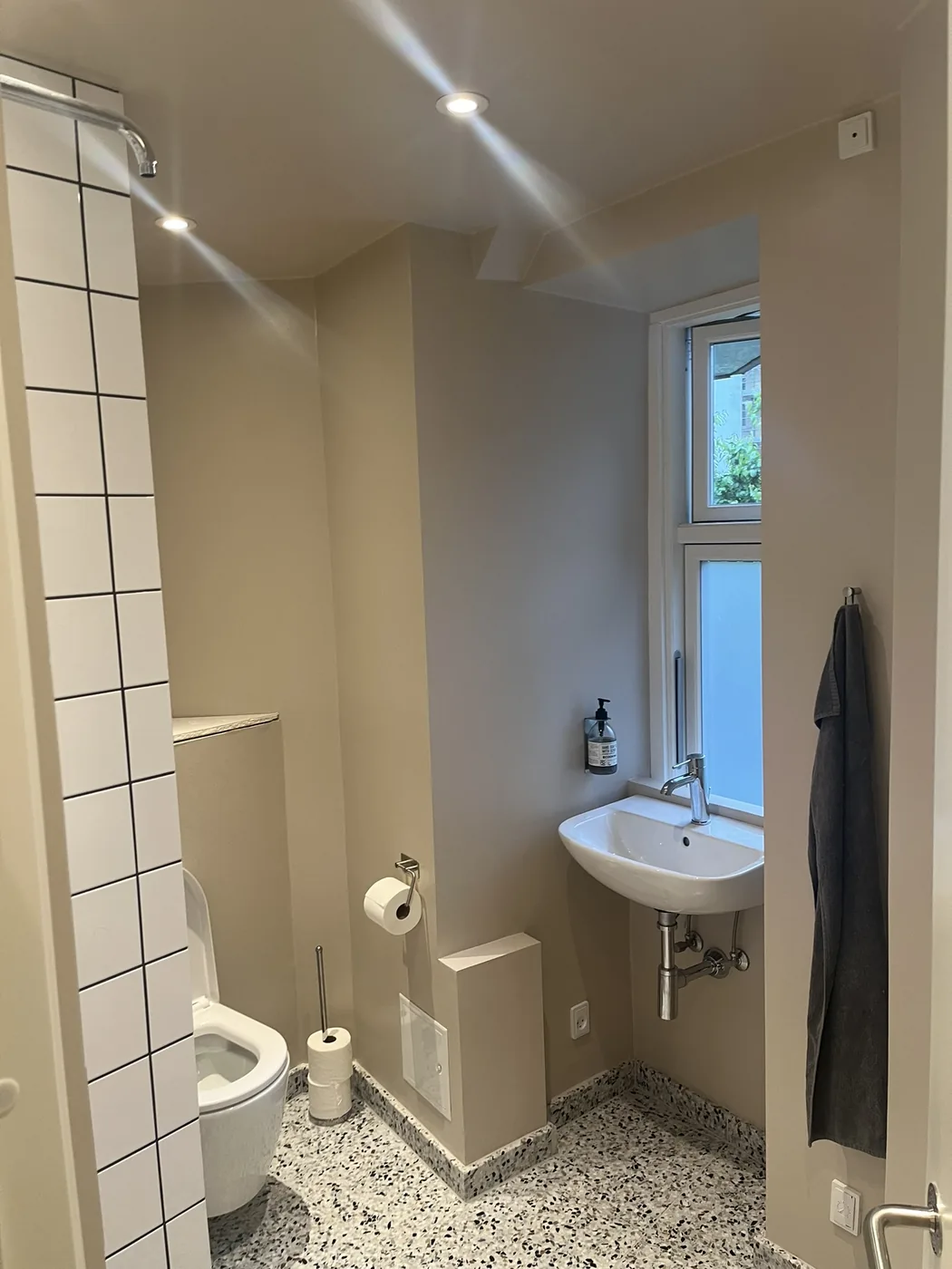 Badeværelse efter renovering med hvide fliser, terrazzogulv og vindue