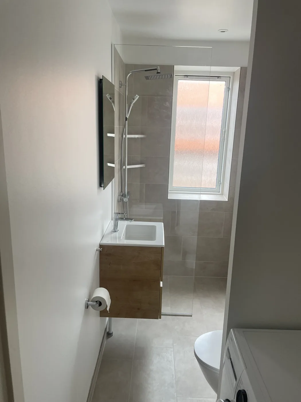 Badeværelse efter renovering med vaskeskab i træ, bruseniche og vindue